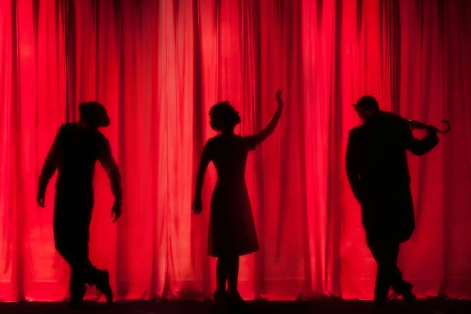 Silhouettes de comédiens devant un rideau rouge
