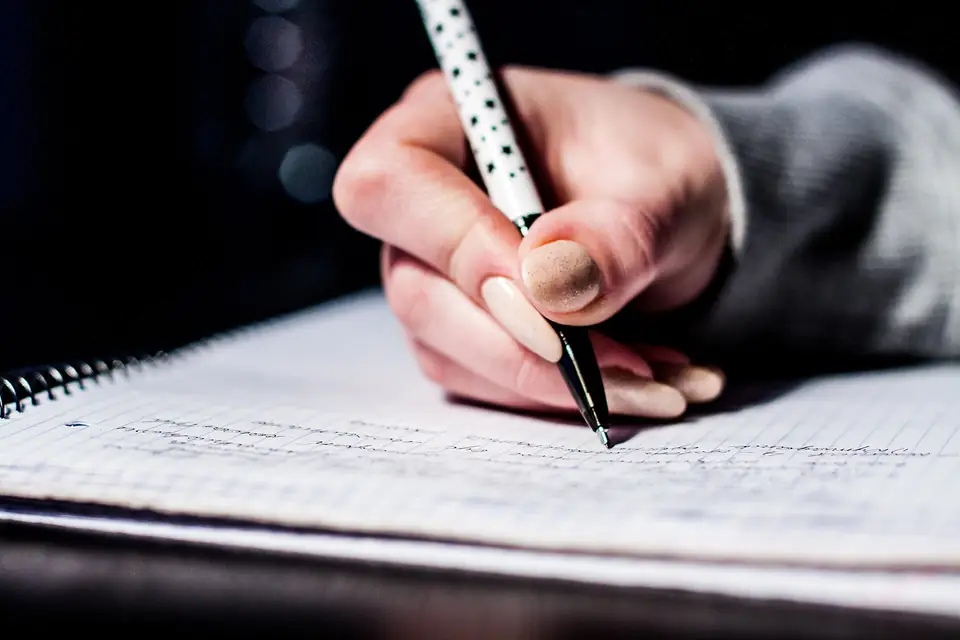 Une main écrit au stylo dans un cahier — l'écrit, au cœur du français